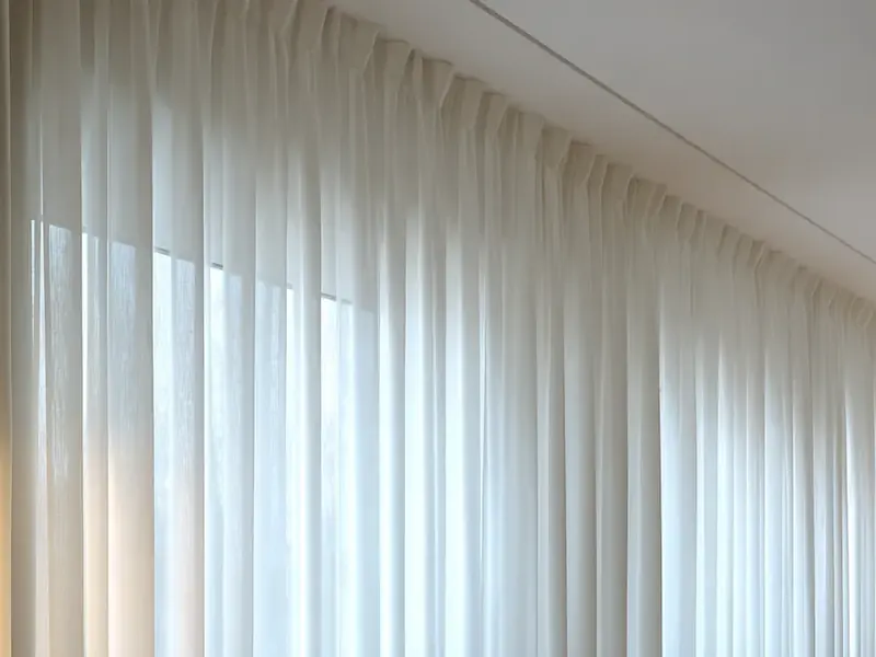 Ceiling-track sheer curtains hanging in even waves across a full window wall