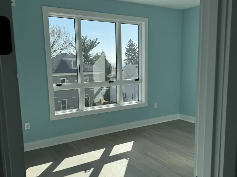 Empty room painted in a soft teal with crisp white window trim and a bare wood floor