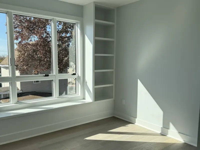Room painted pale sage with built-in shelving beside a bright window reveal